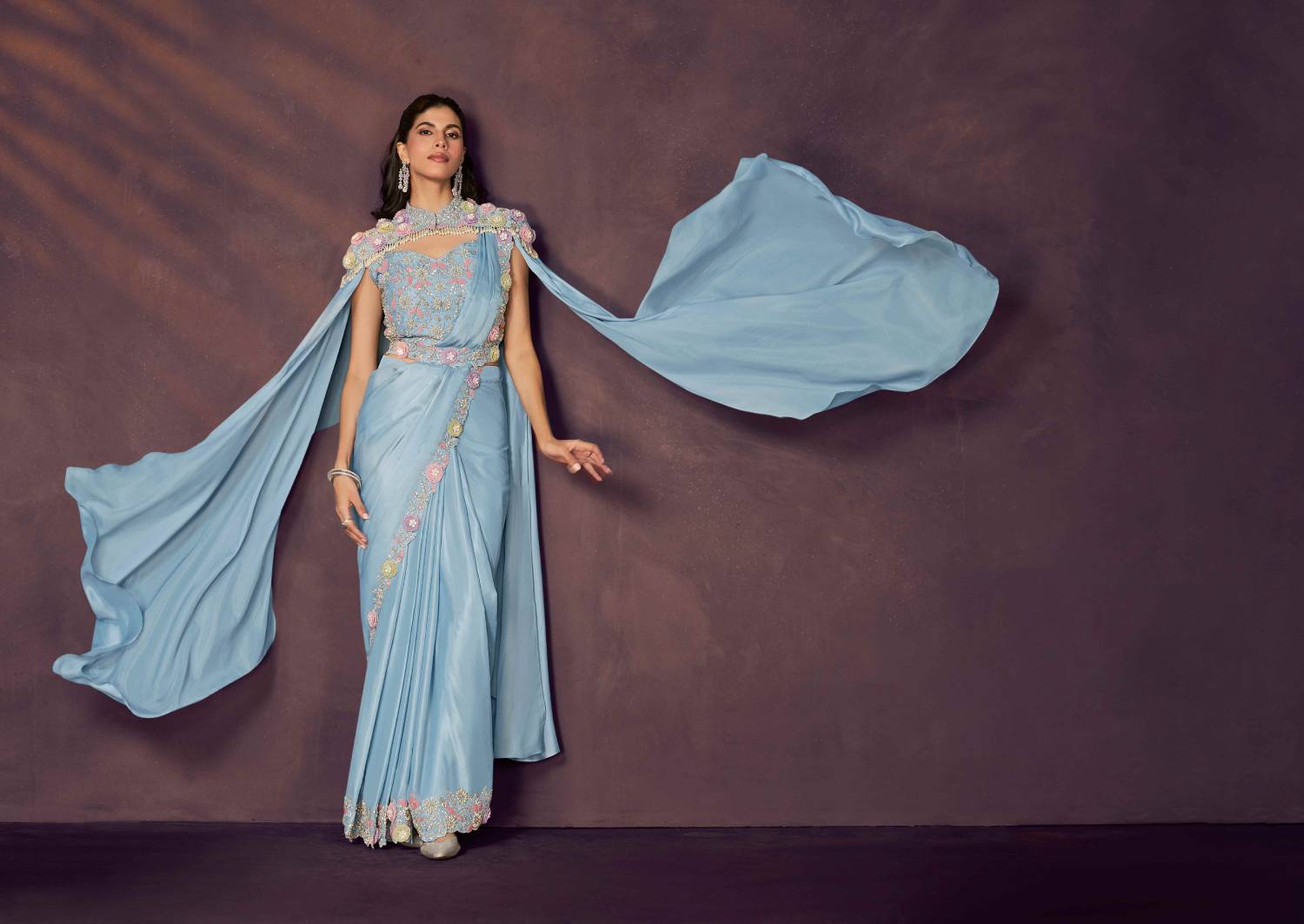 Woman in a light blue saree with a flowing fabric against a dark background