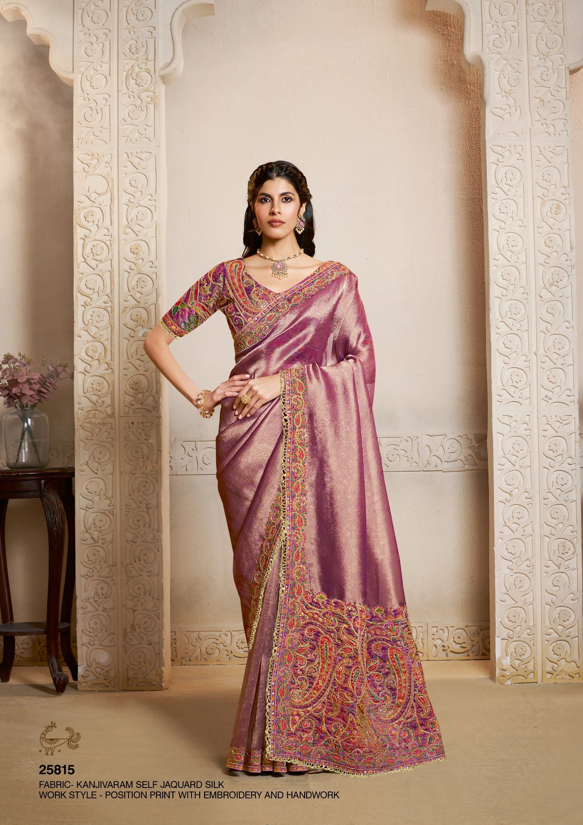 A woman models a purple silk saree with intricate gold, orange, and red paisley embroidery along the border and sleeves.