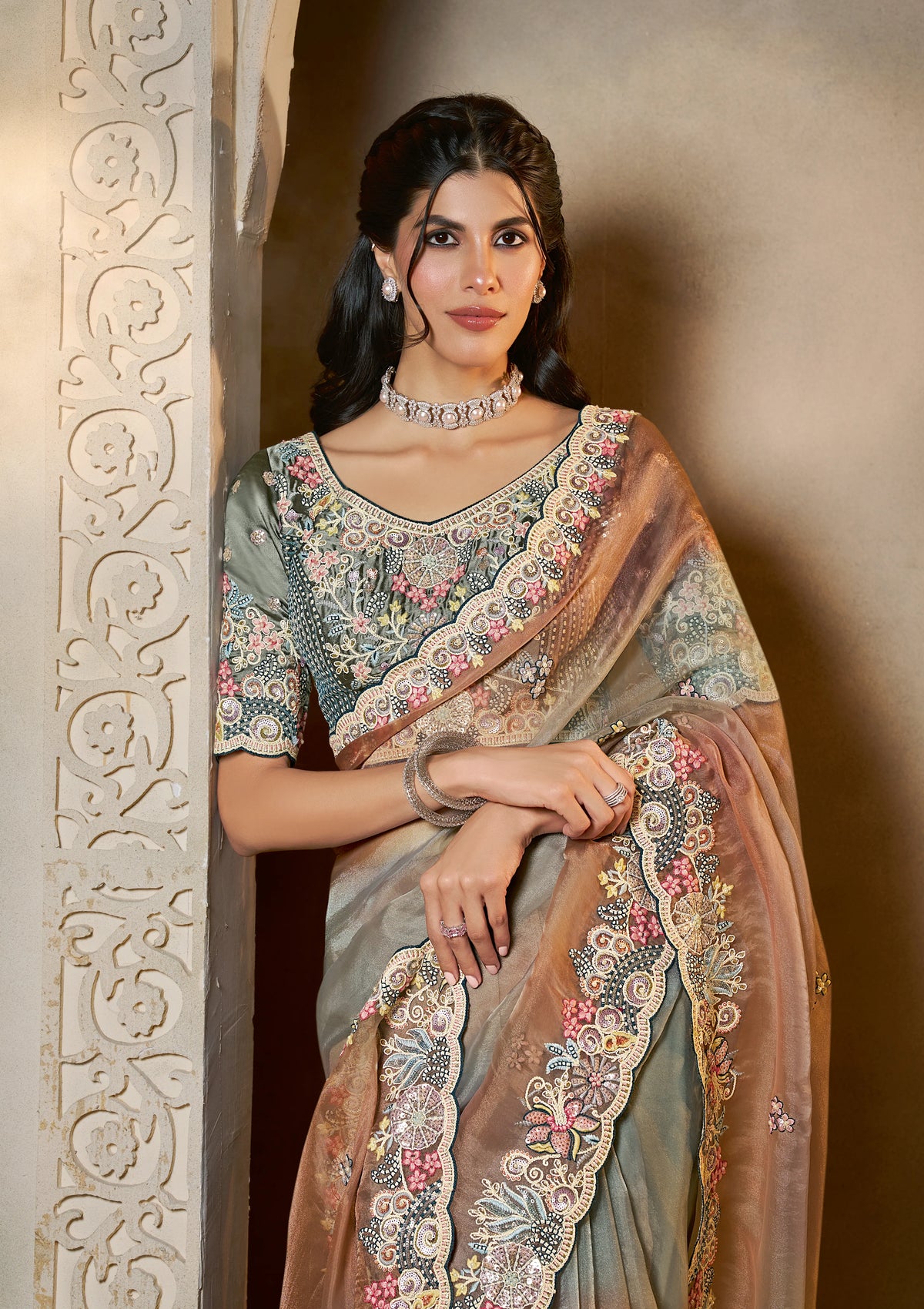 Woman wearing a traditional saree with intricate patterns, standing against a neutral background.