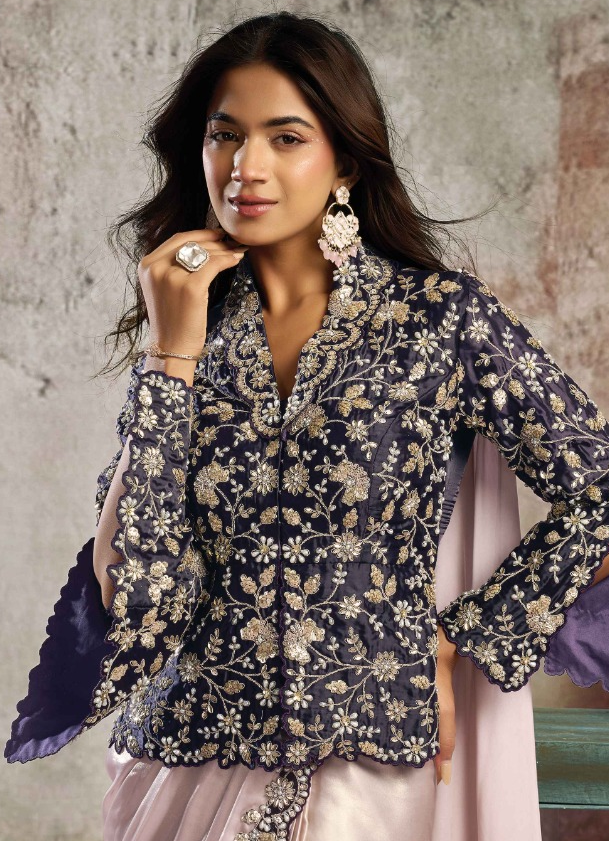 A woman models a dark navy blue embroidered kurta with beige floral patterns, paired with a light pink skirt, against a textured gray wall background.