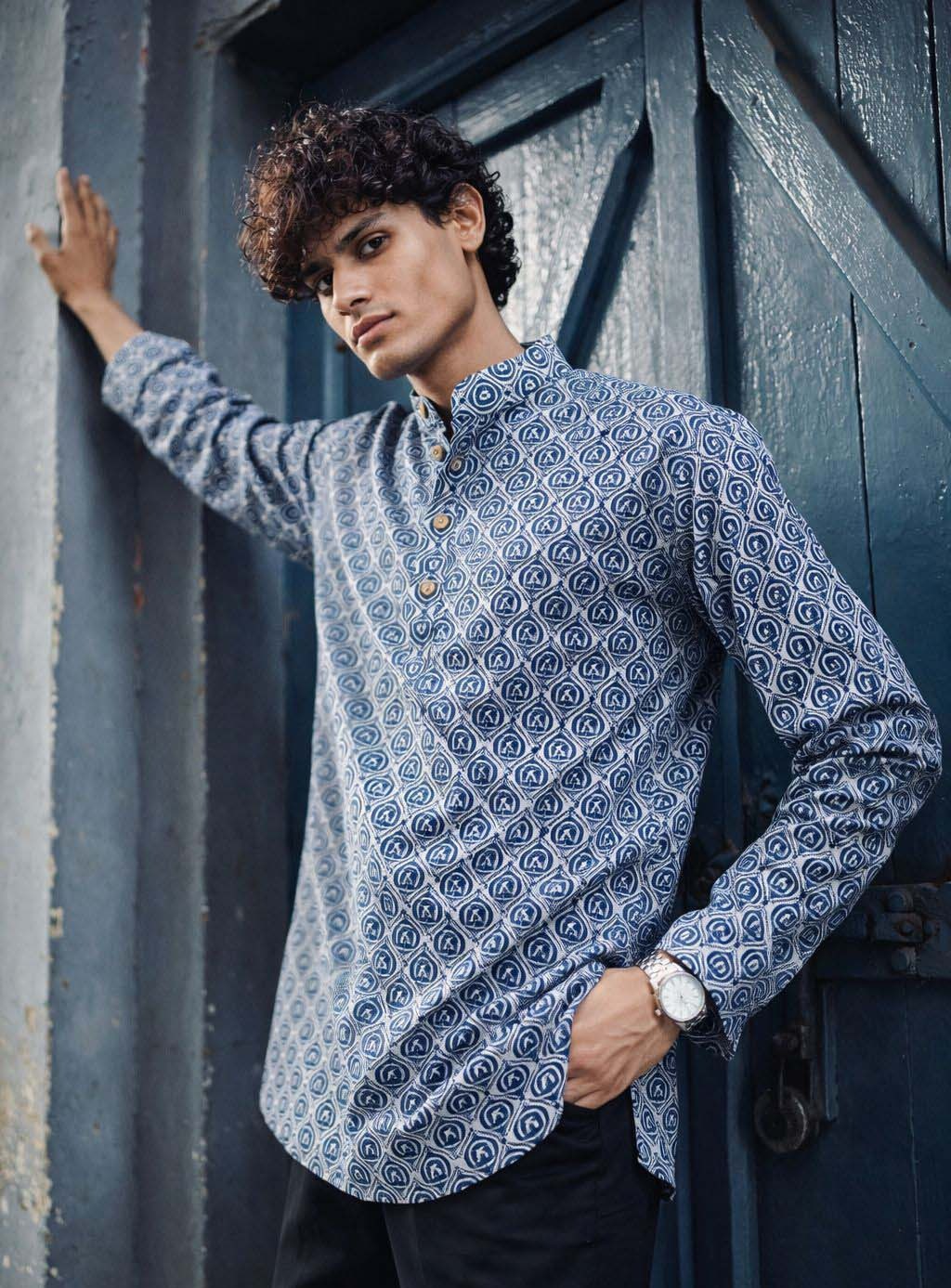 A man wearing a blue and white patterned long-sleeve kurta leans .