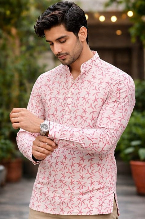 A man wearing a light pink long-sleeve kurta with a red abstract pattern,.