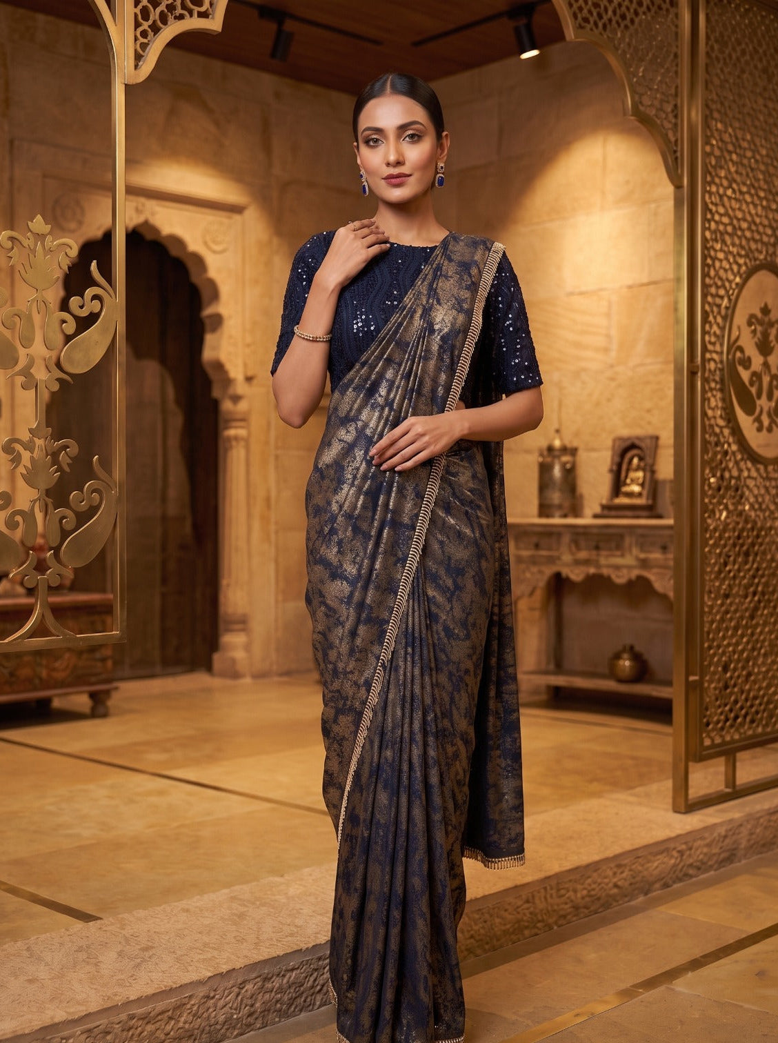A woman modeling a dark navy blue saree with a subtle gold-toned pattern and a matching embellished blouse