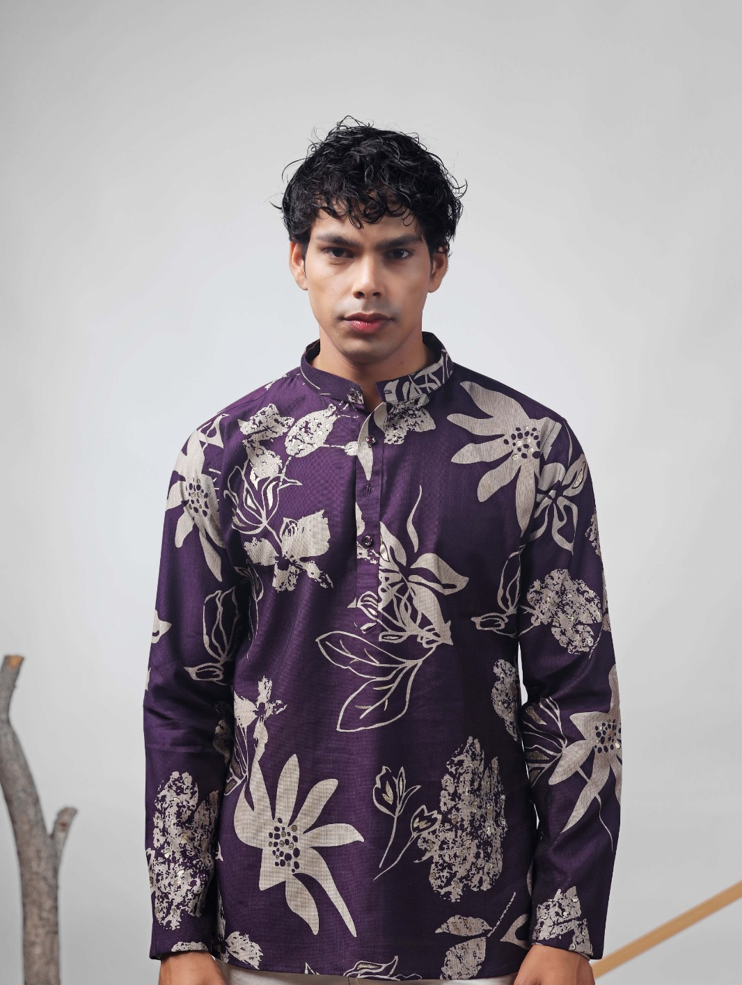 A man wearing a purple long-sleeve kurta with a large white floral print, standing against a light gray studio background.